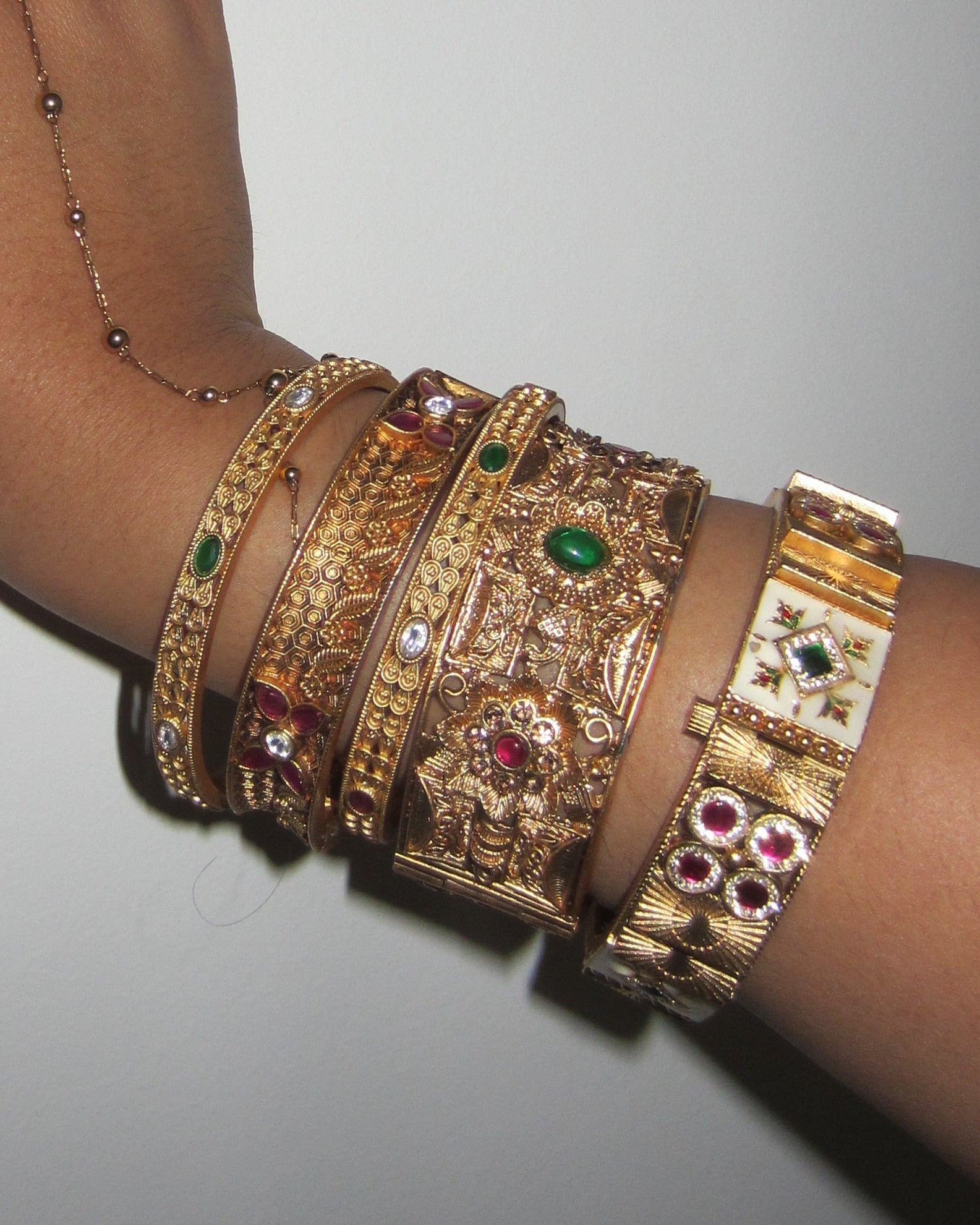 Hand wearing multiple gold bracelets with gemstones on a gray background