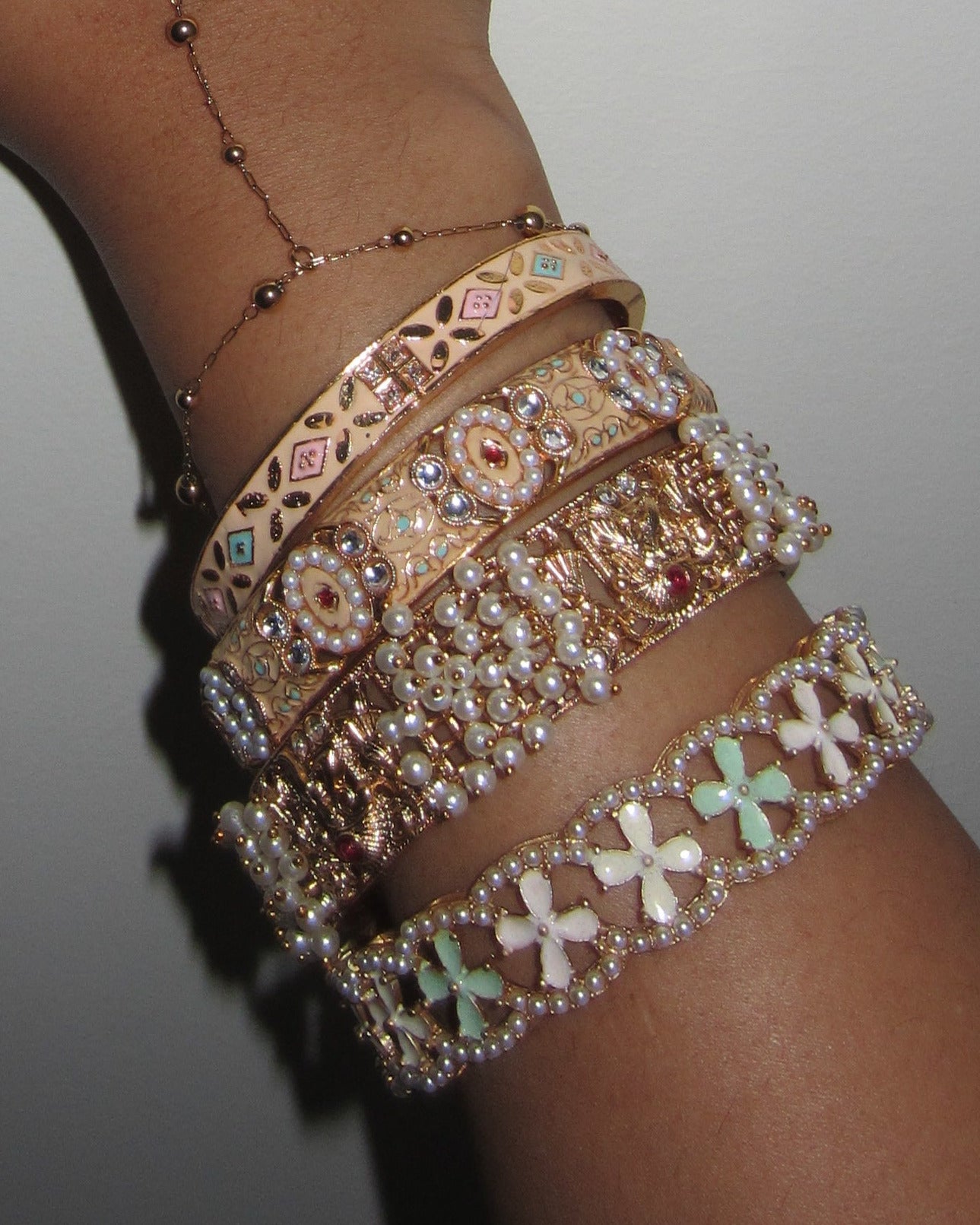 Hand wearing multiple gold bracelets on a plain background