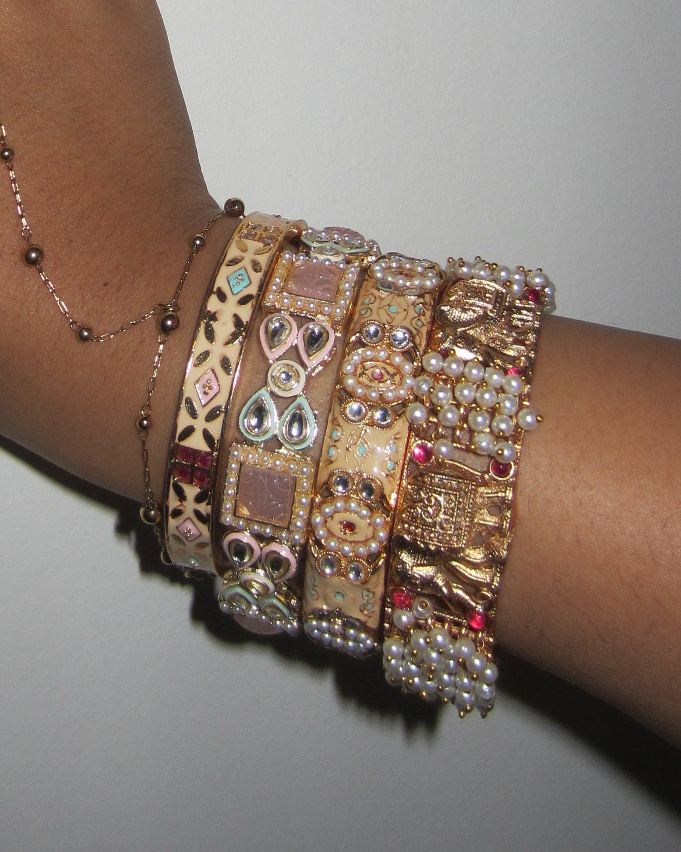 Hand wearing multiple gold bracelets on a plain background