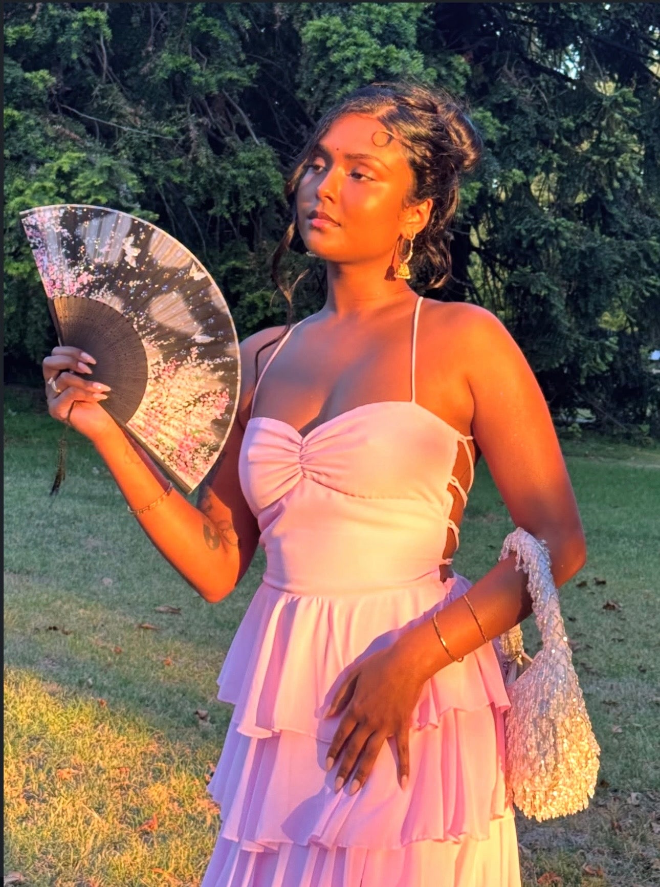 Woman in a pink dress holding a decorative fan outdoors