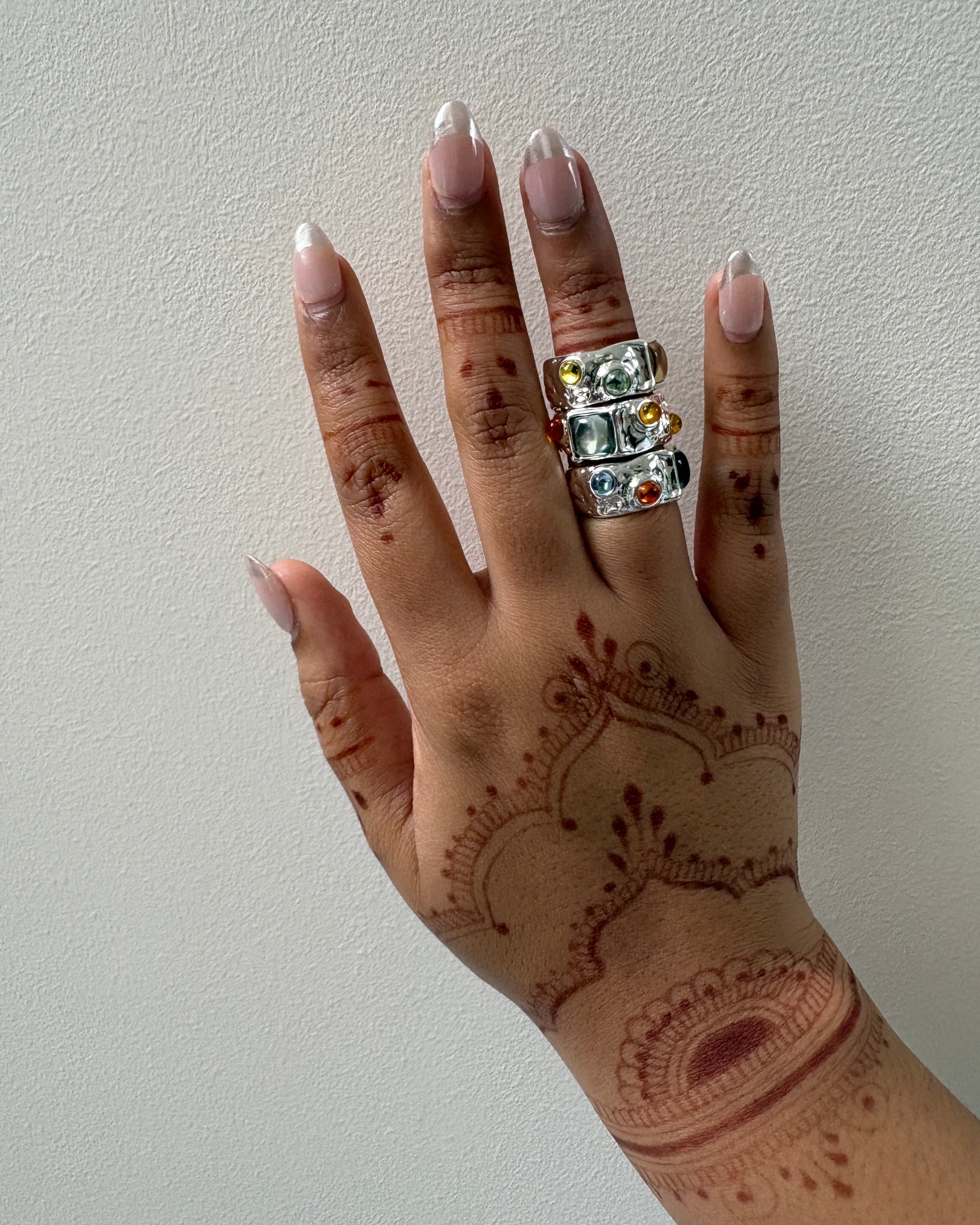 Hand with henna design and multiple rings on a plain background