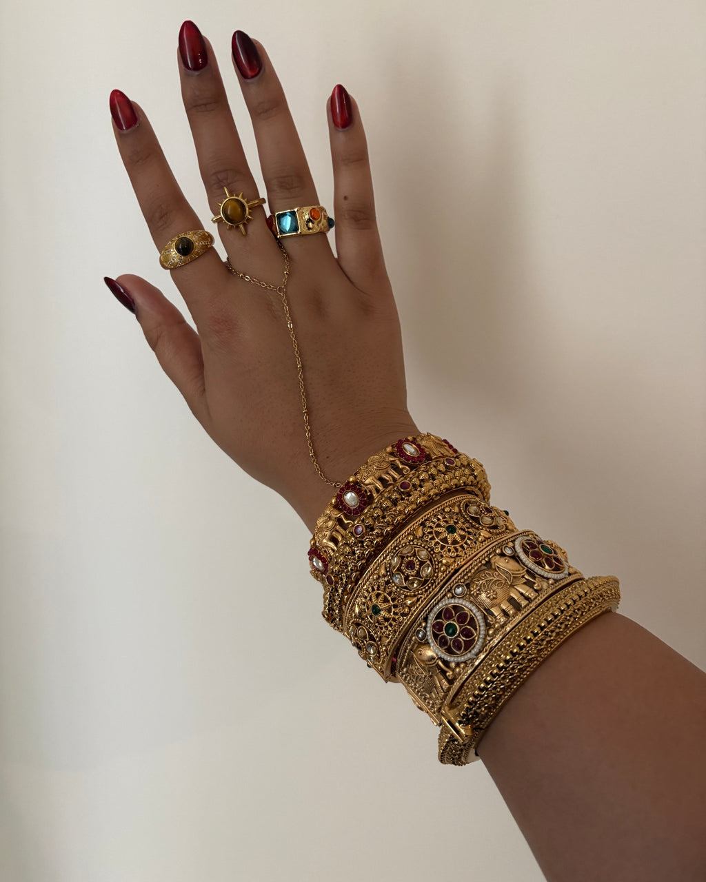 Hand wearing gold jewelry with intricate designs on a neutral background