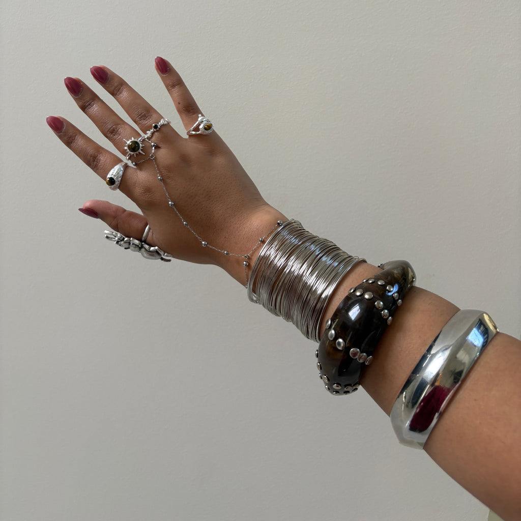 Hand wearing multiple silver bracelets and rings on a plain background