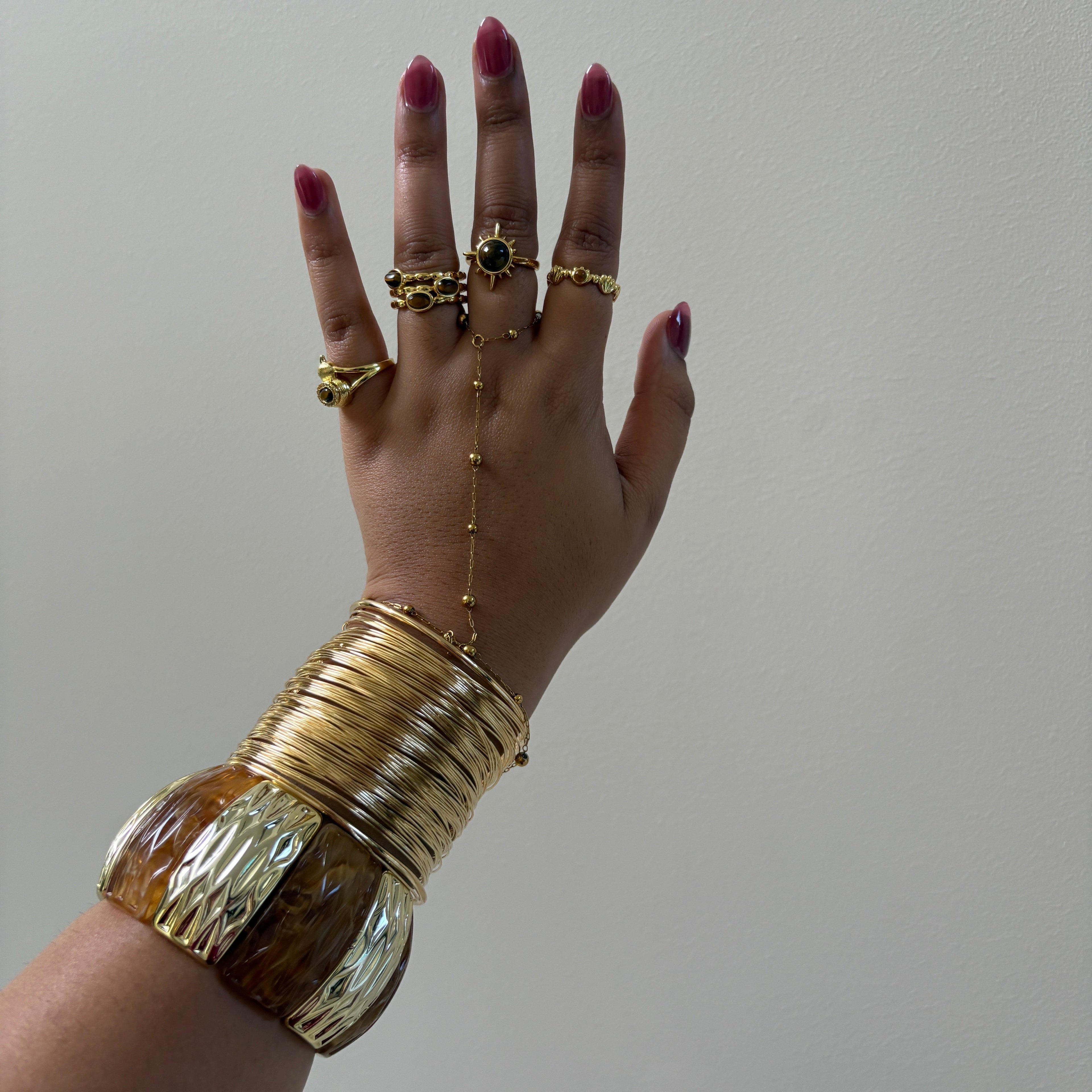Hand wearing gold rings and bracelets against a plain background