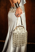 Person holding a decorative handbag with intricate patterns and fringe details.