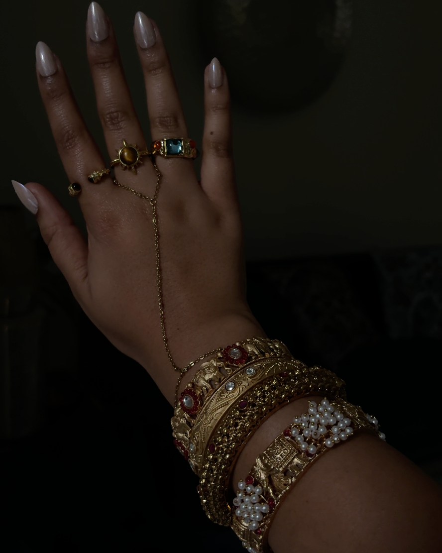 Hand adorned with gold jewelry on a dark background